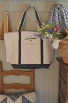Natural canvas boat tote with navy trim and embroidered Homemaker’s Club logo